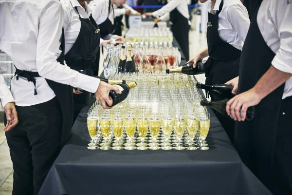 Servis häller upp mousserande vin i glas. Galamiddag.